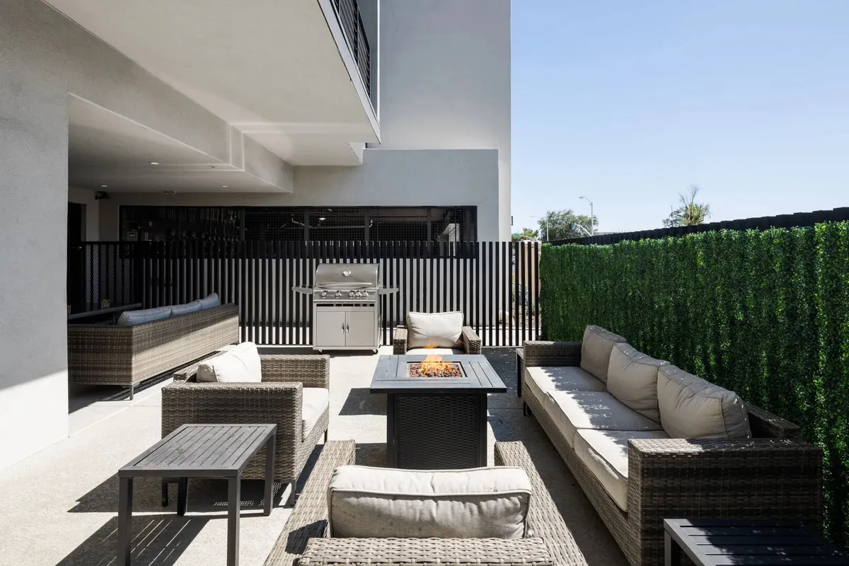 A stylishly designed outdoor area featuring a glowing fire pit, comfortable seating, a grill for barbecuing, and lush greenery. The setup encourages evening relaxation, cookouts, and social events beneath the stars.