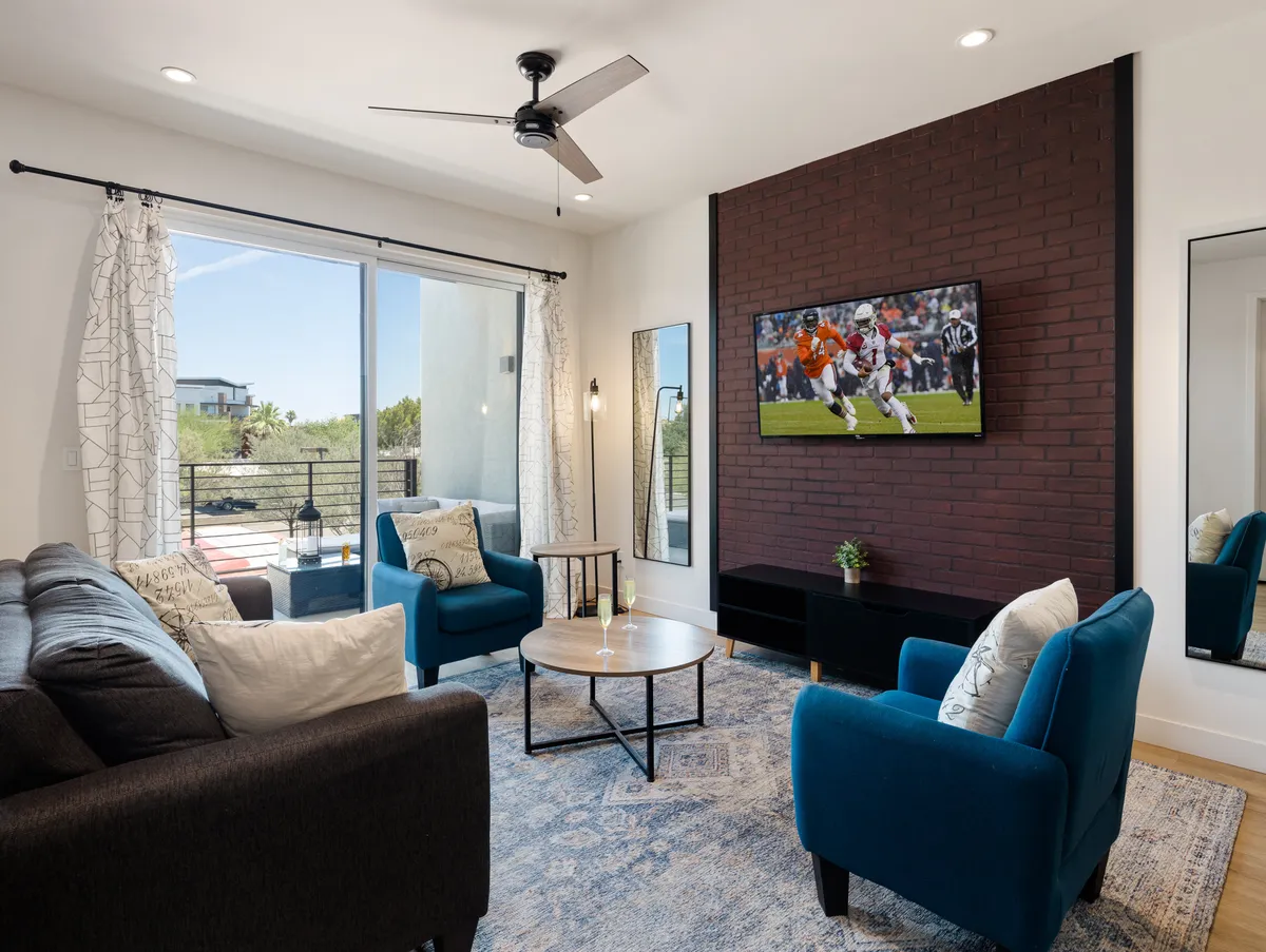 A comfortable living room featuring a plush sofa, blue accent chairs, a TV mounted on a brick wall, and a coffee table—arranged for socializing or watching TV.