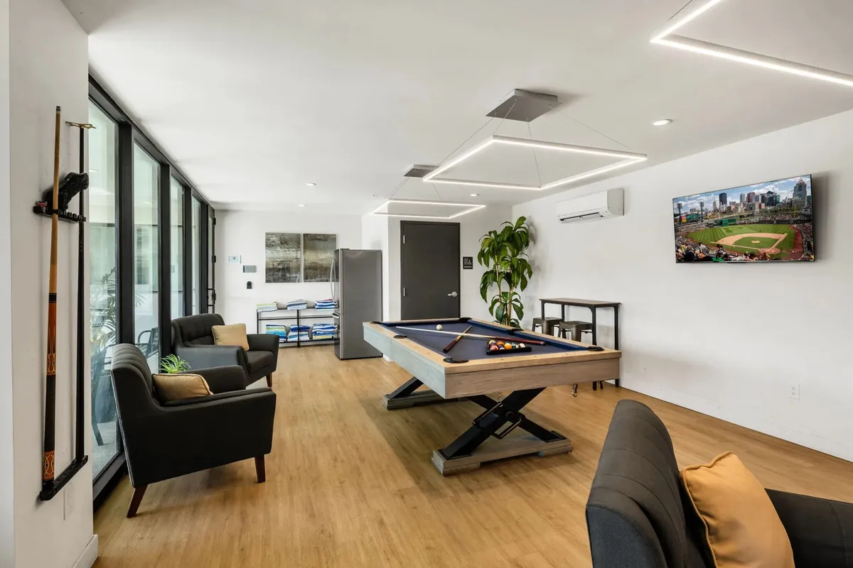 An inviting interior space with a pool table, plush sofas, a large television, and greenery, creating a lively yet comfortable atmosphere ideal for relaxing, socializing, or catching a game indoors.
