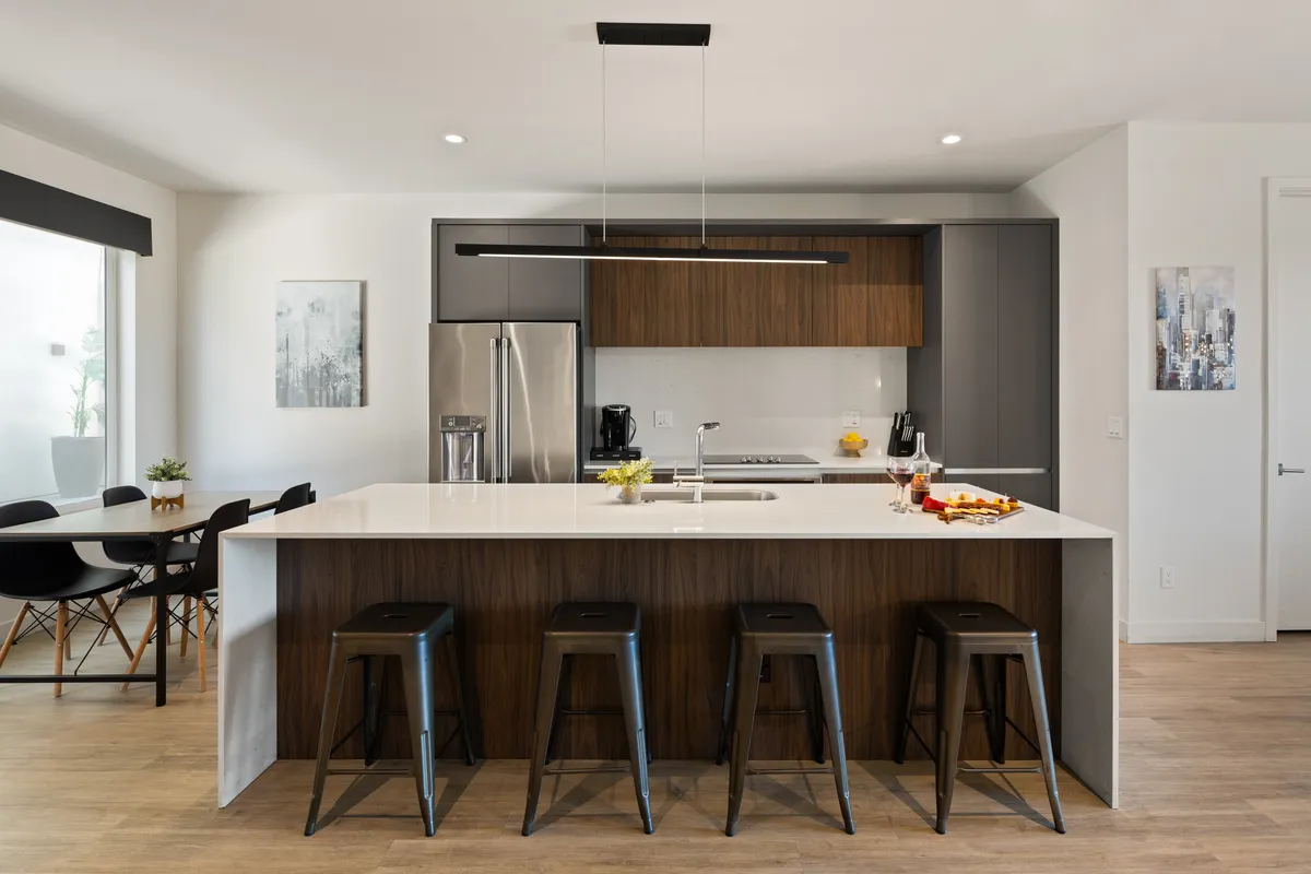 A sleek, functional kitchen showcasing a spacious island with bar stools, a stainless steel refrigerator, and modern cabinetry. The scene exudes a welcoming vibe, perfect for preparing meals or enjoying morning coffee.