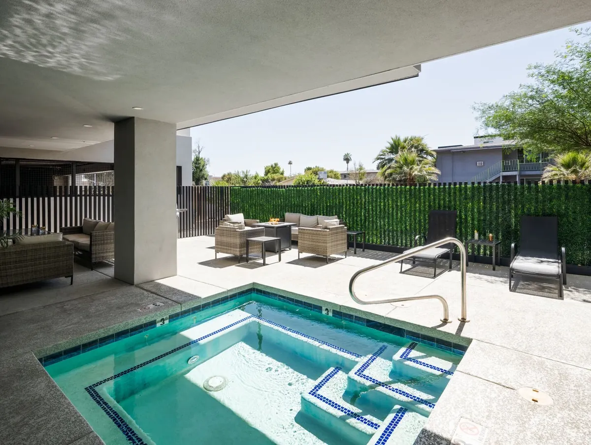 A tranquil spa area with mosaic tiles, plush outdoor seating, and lush greenery complemented by tall palm trees in the background. The setting radiates relaxation and offers an inviting oasis for residents to unwind between urban adventures.