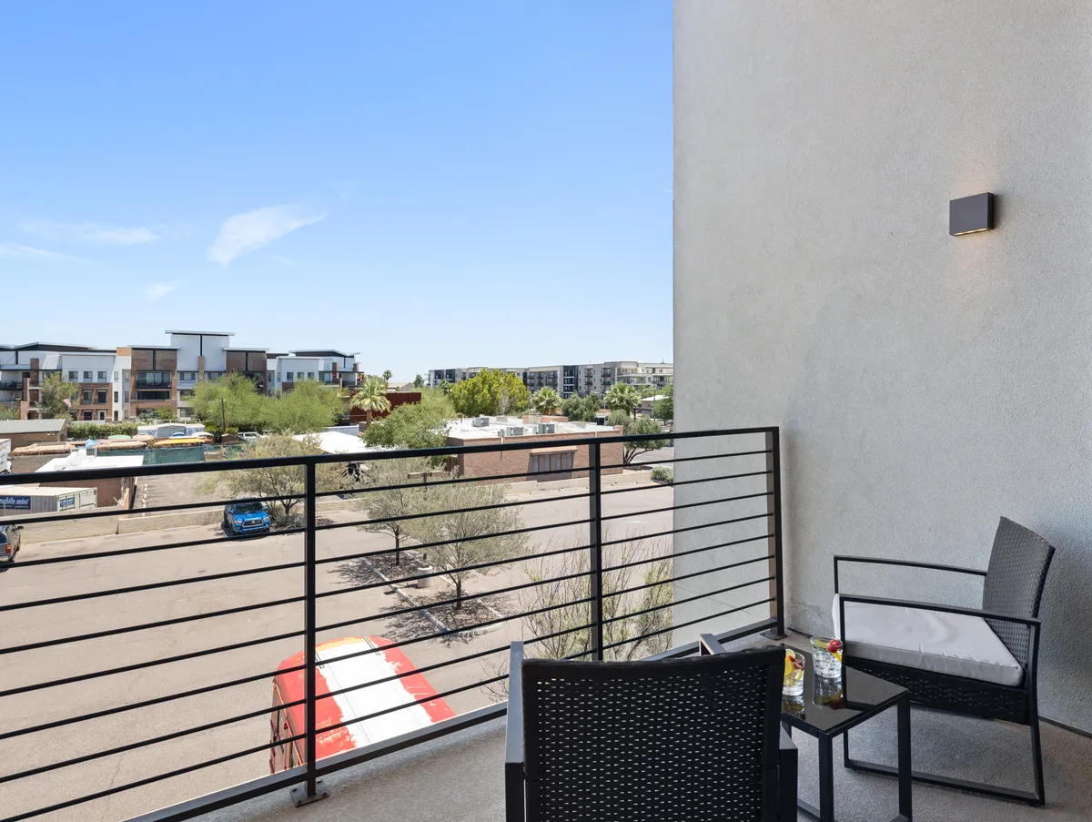 A tranquil private balcony with two chairs and a small table, overlooking distant buildings and an open blue sky—an inviting spot to enjoy fresh air or morning coffee.